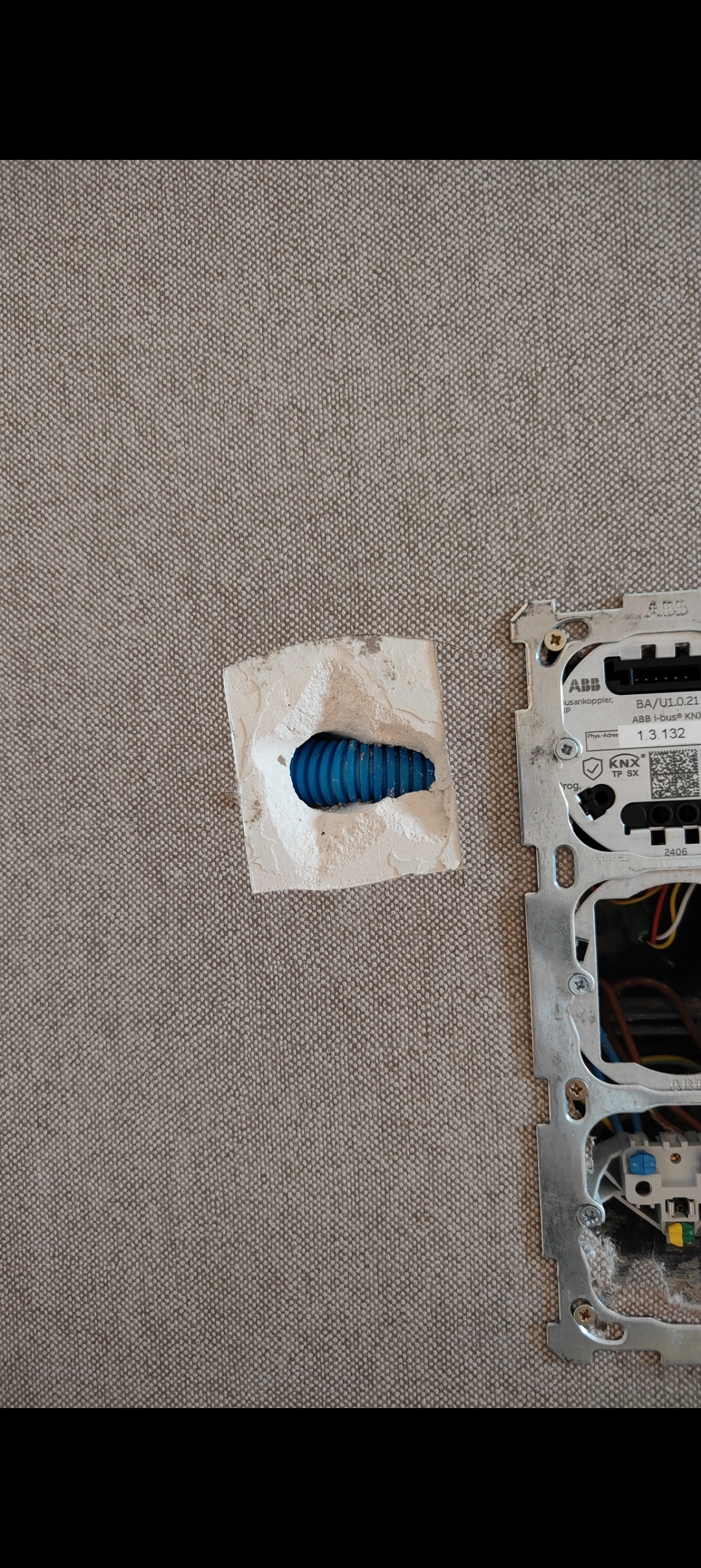 Freigelegte Schadstelle in einer grauen Tapete neben einer geöffneten Elektroinstallation.
